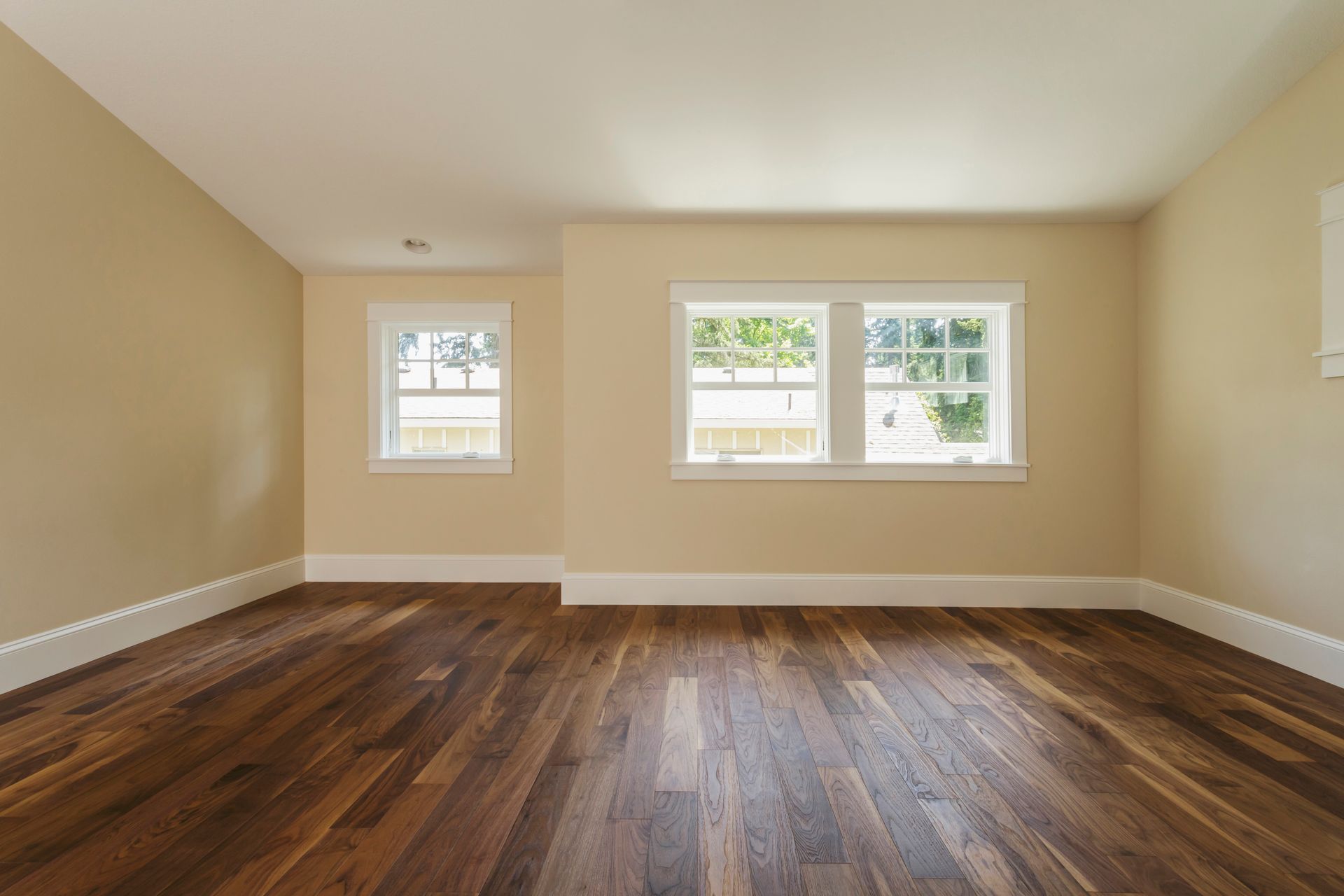 An empty room with hardwood floors and two windows.