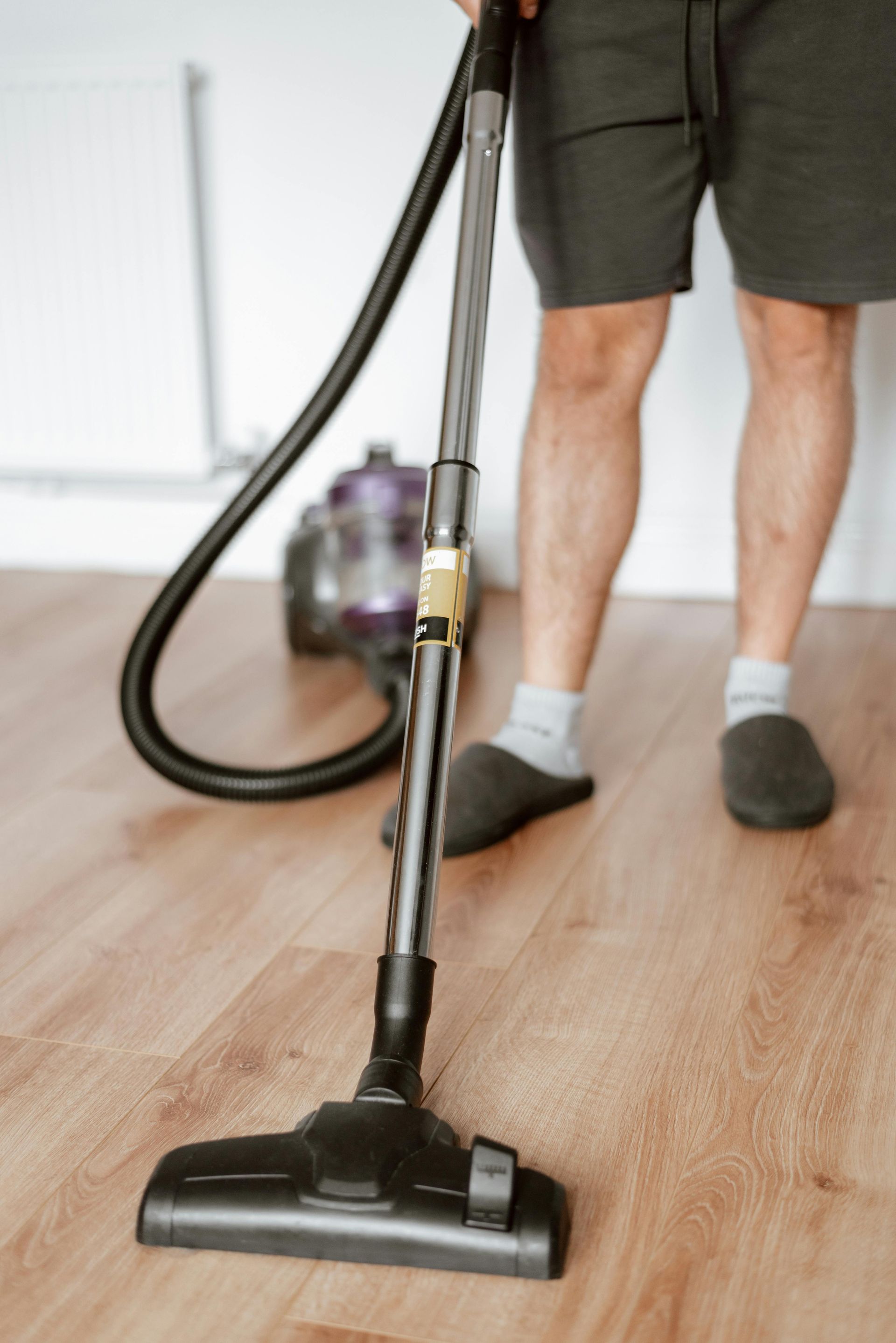 Person vacuuming hardwood floor with canister vacuum cleaner as part of regular floor maintenance