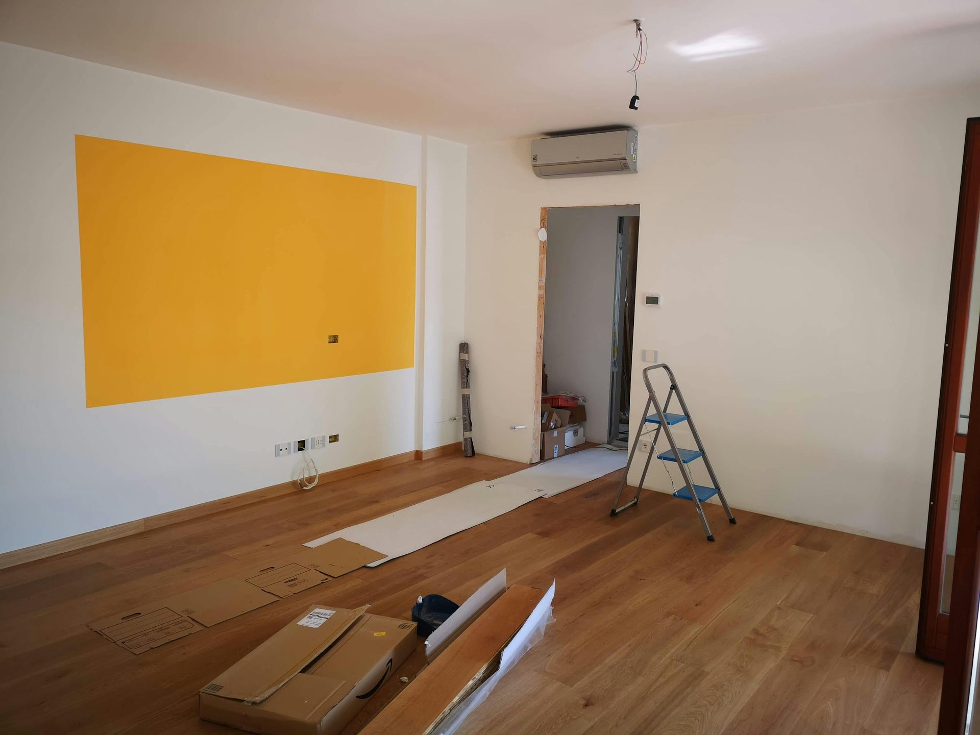Hardwood floor installation in progress in empty room with painting supplies and ladder