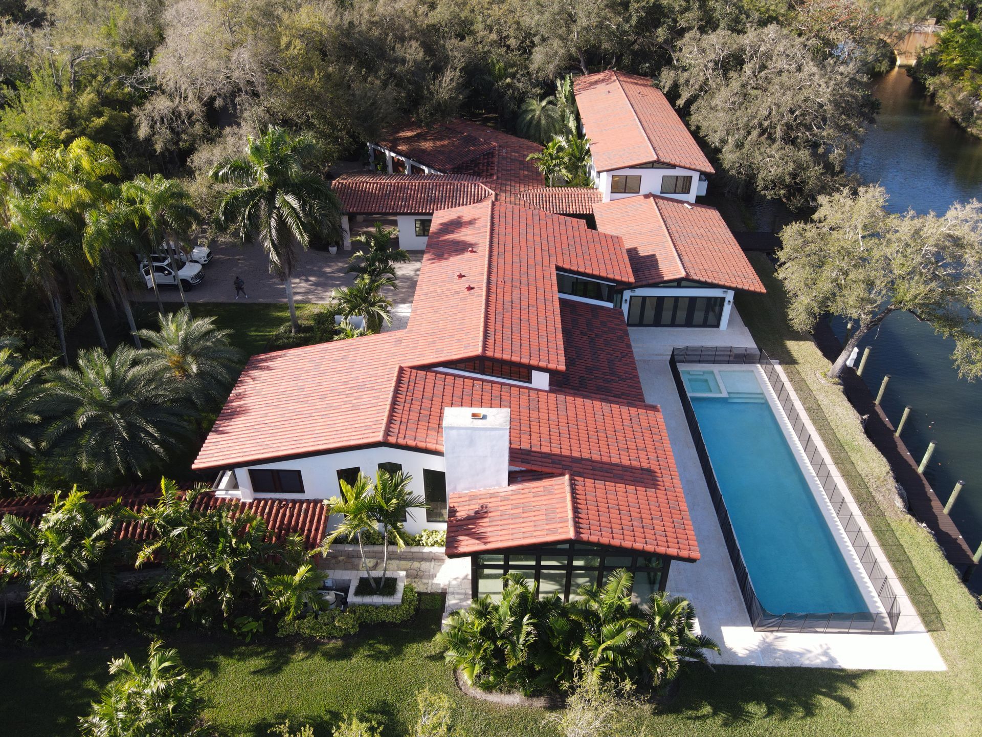 Vista aérea de una casa de estuco blanco con techo de tejas rojas y una larga piscina junto a un canal.