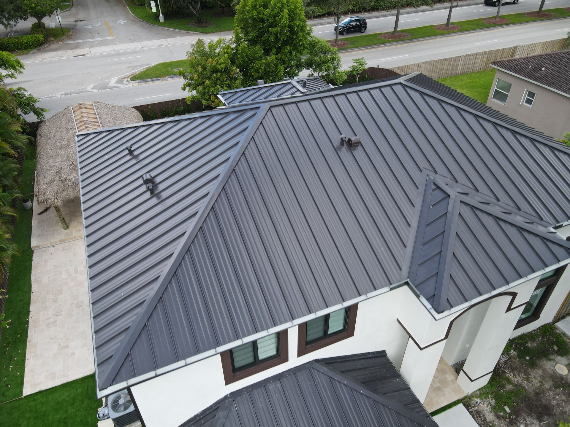 Techo de metal gris en una casa blanca con entrada circular y una pequeña cabaña tiki.
