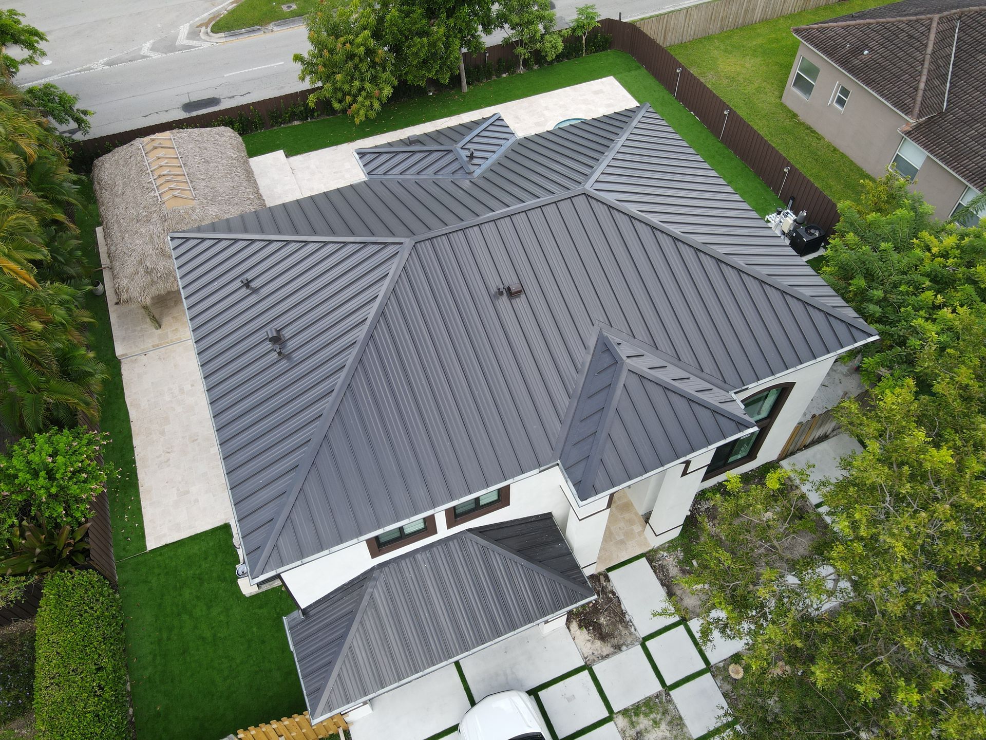 Vista aérea de una casa moderna con techo de metal gris oscuro, rodeada de césped verde y árboles.