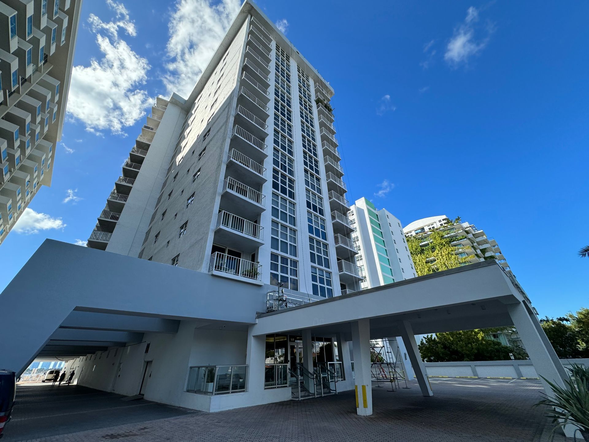 Un edificio alto, blanco y de gran altura, con una entrada cubierta y un cielo azul de fondo.