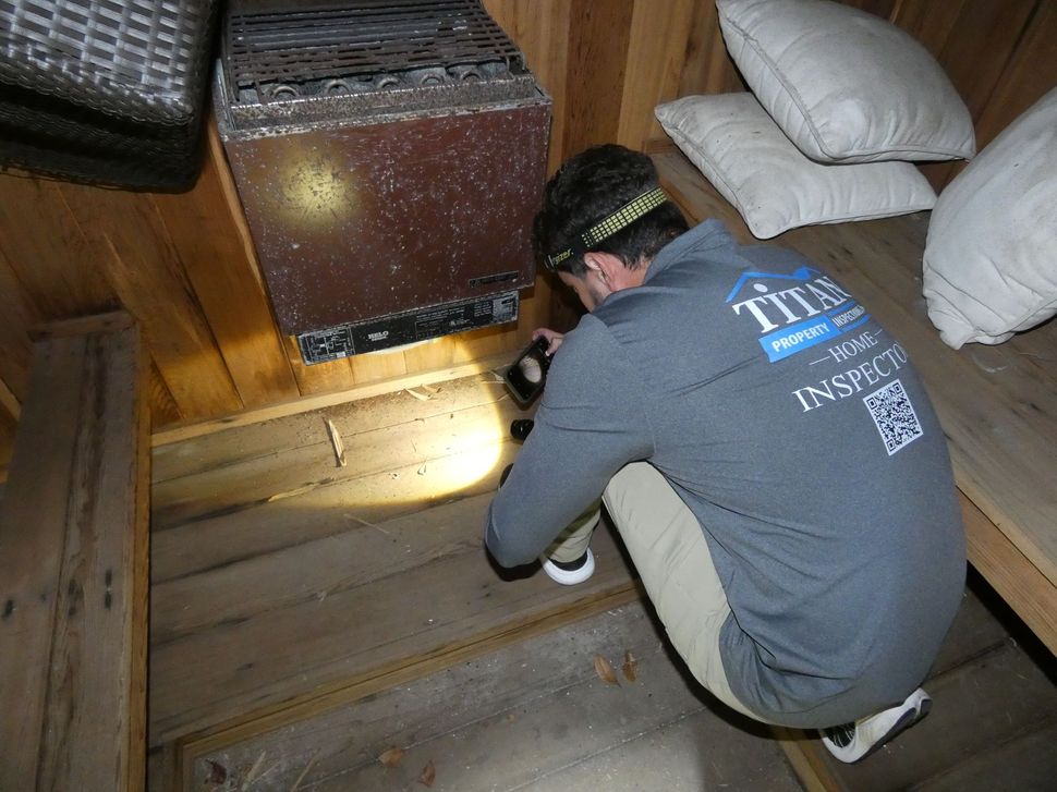 Man inspecting sauna interior with a flashlight. Wooden benches, heater, and pillows visible.