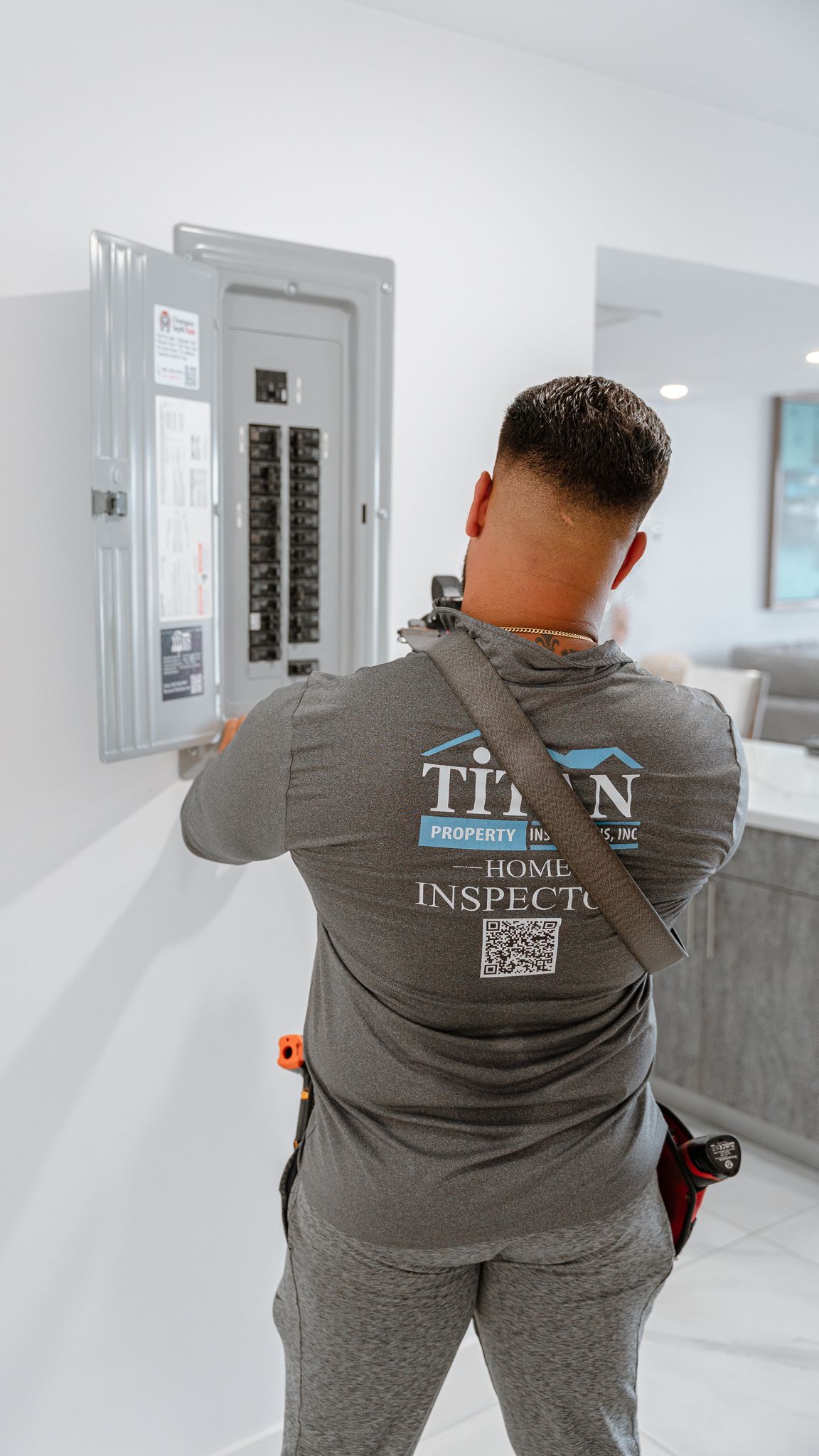 Electricista trabajando en un cuadro eléctrico en interiores. Camisa gris y cinturón de herramientas.