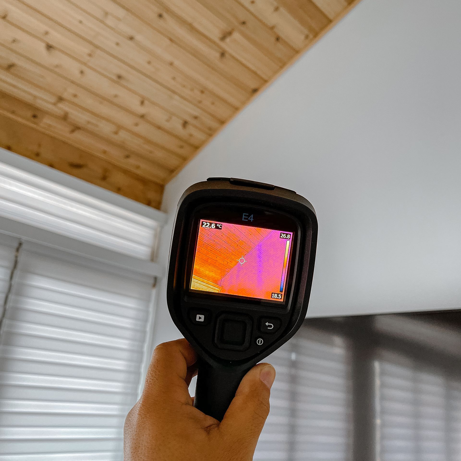 Mano sosteniendo una cámara térmica apuntando al techo blanco; la pantalla muestra variaciones de calor.
