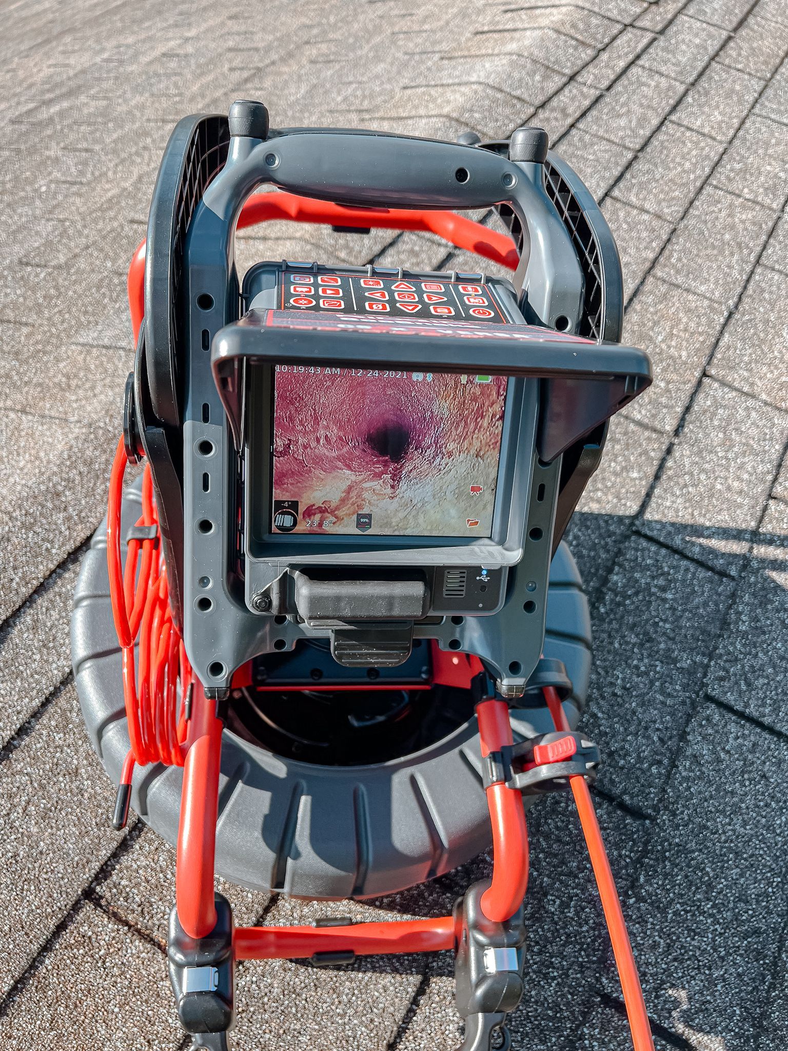 Cámara de inspección en un tejado que muestra el interior oscuro de una tubería. Dispositivo rojo y gris sobre tejas.