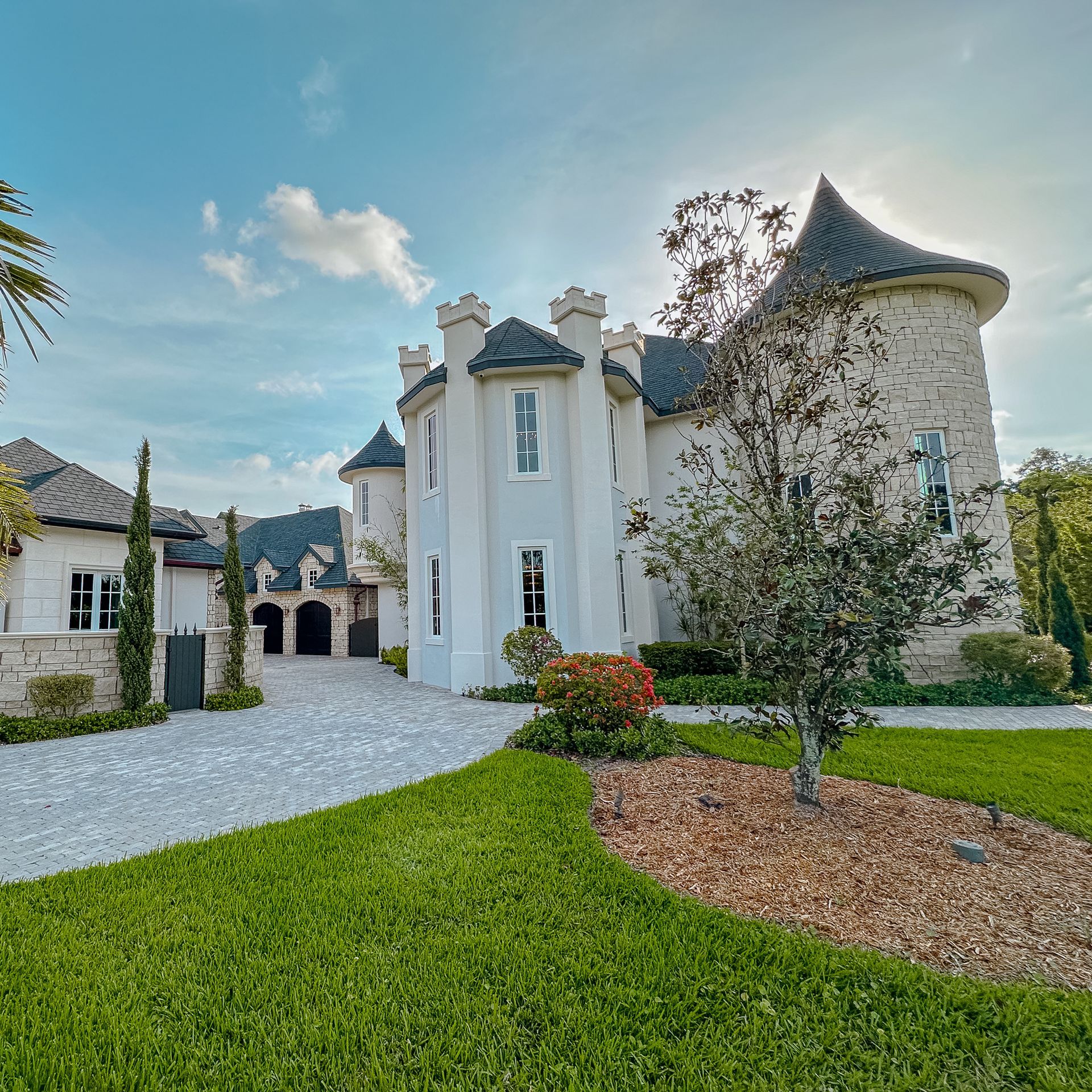 Casa estilo castillo de piedra blanca con torre circular, puerta arqueada y camino de grava.