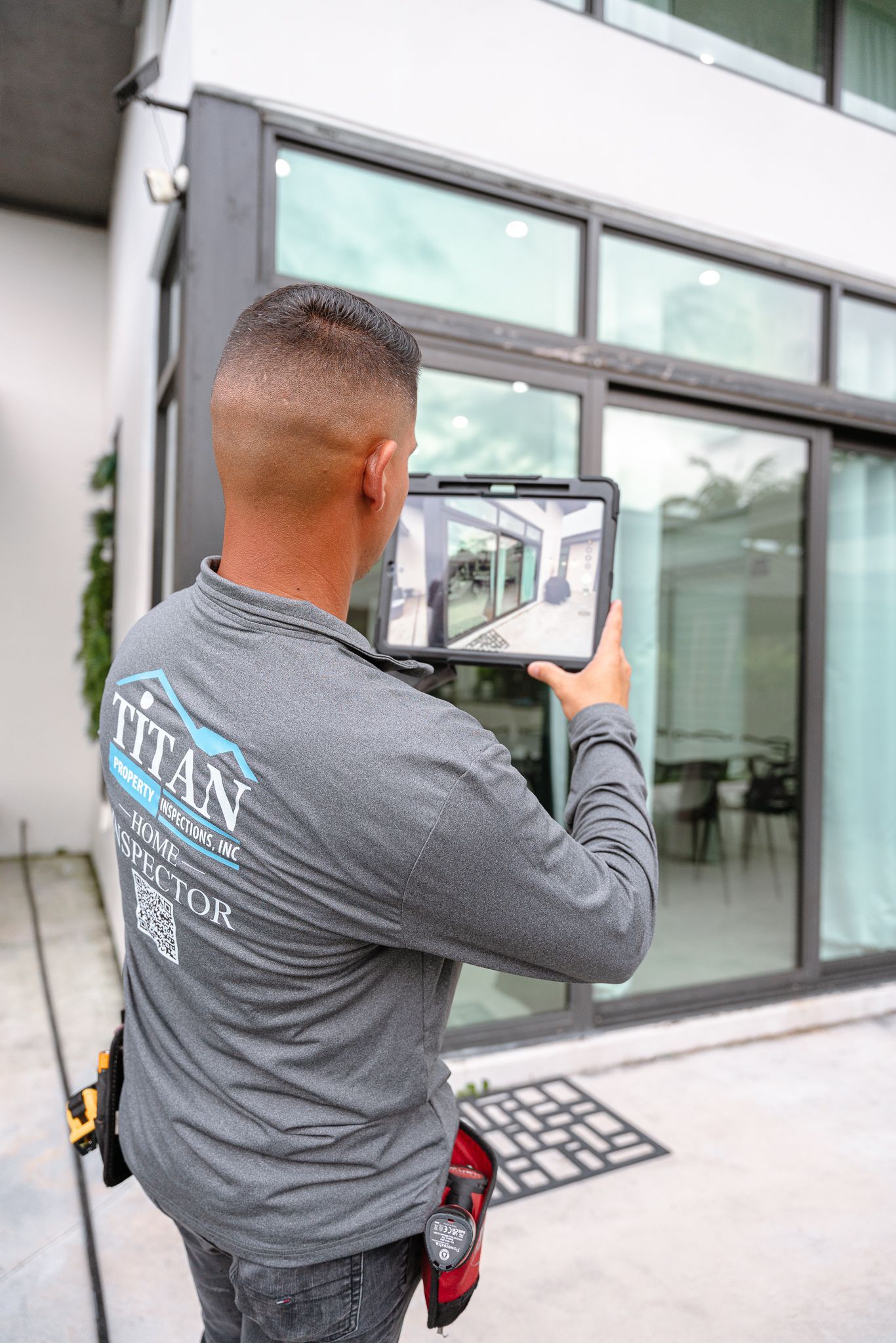 Un hombre con camisa gris usa una tableta frente a una puerta corrediza de vidrio.