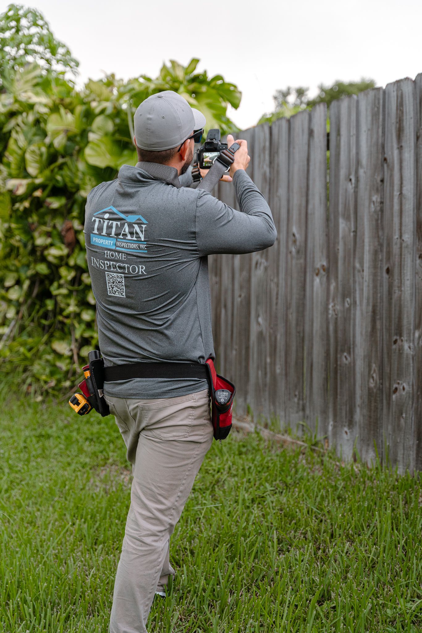 Persona que viste una camisa gris fotografía una valla de madera en un patio cubierto de hierba.