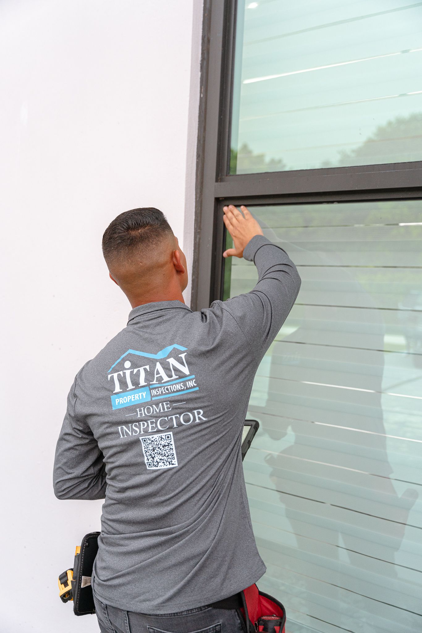 Hombre instalando una lámina para ventanas en un edificio. Camisa gris con el logo. Foto exterior.