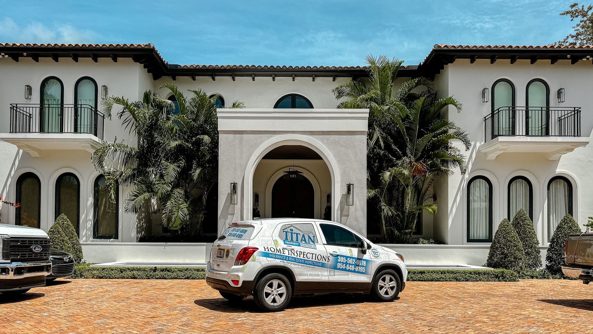 White SUV parked in front of a white mansion with arched windows and a palm tree.