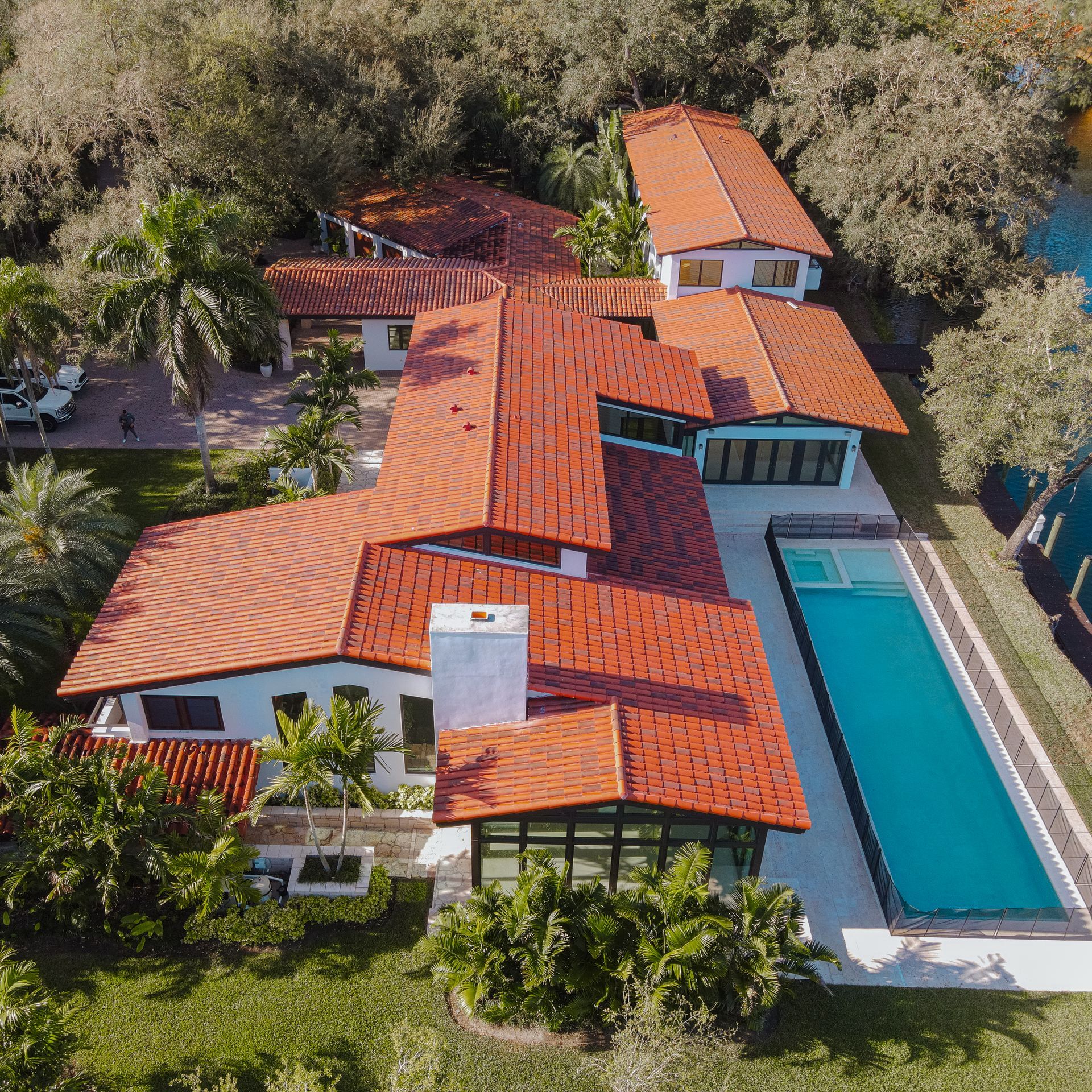 Vista aérea de una gran casa blanca con techo de tejas rojas y una larga piscina rectangular.