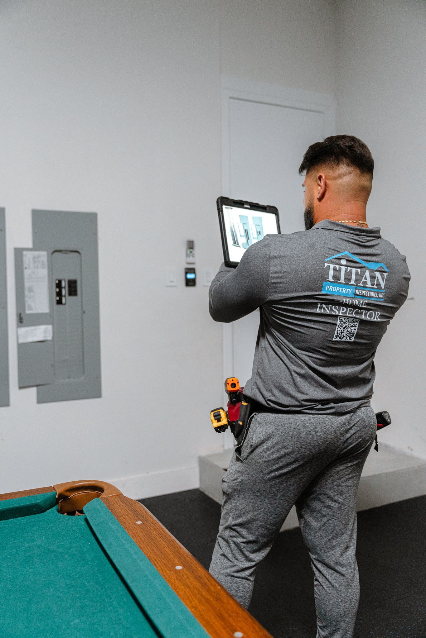 Un hombre con uniforme gris usa una tableta en una habitación con una mesa de billar y un panel eléctrico.