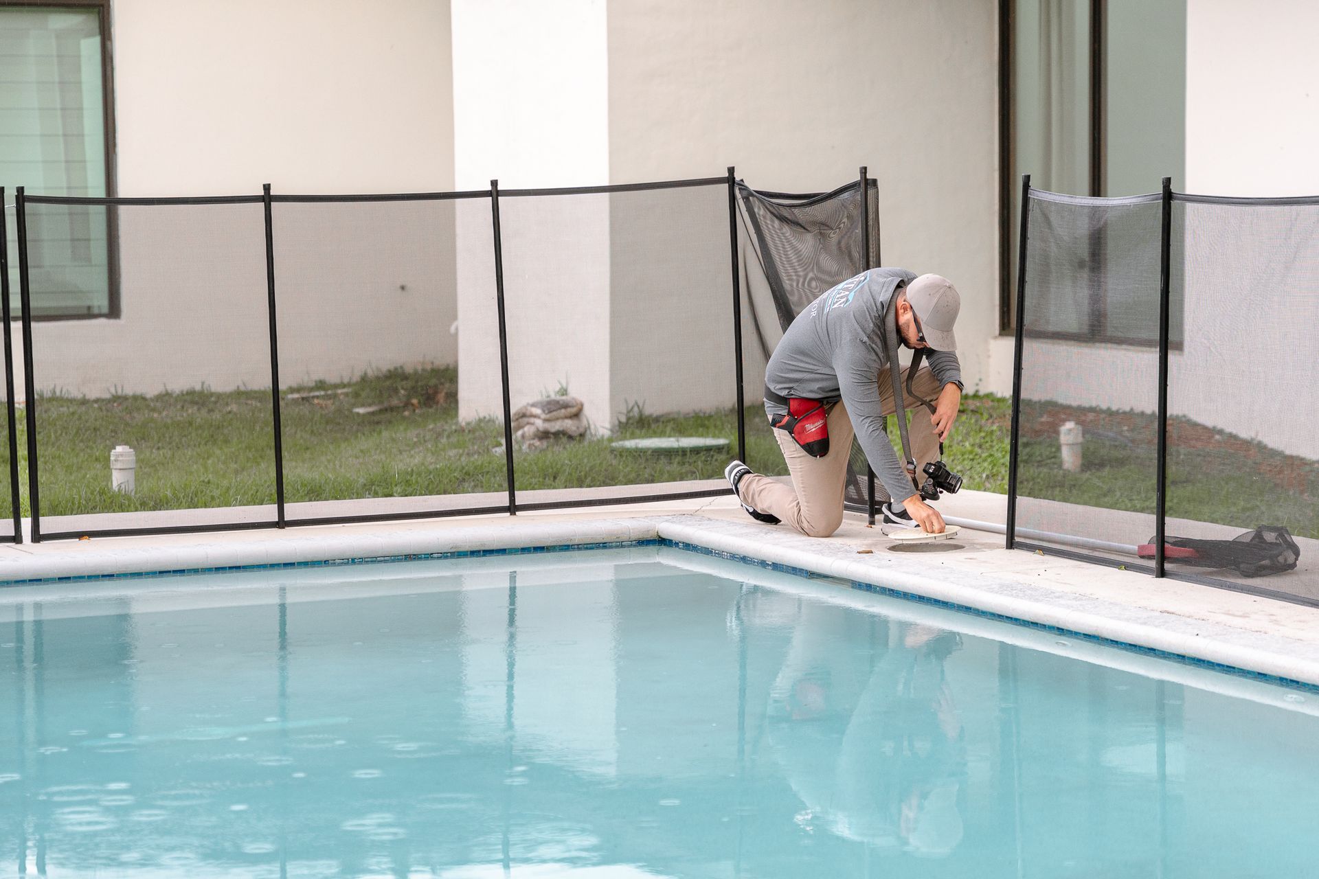 Persona instalando una valla de seguridad de malla negra alrededor de una piscina.