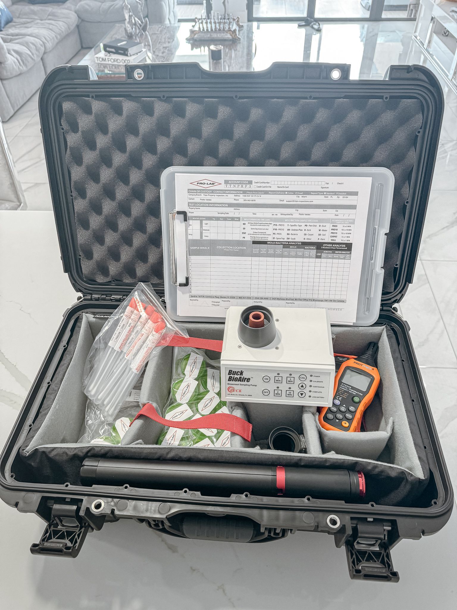 Estuche rectangular negro abierto con diversas herramientas de topografía, documentos y un dispositivo portátil de color naranja.