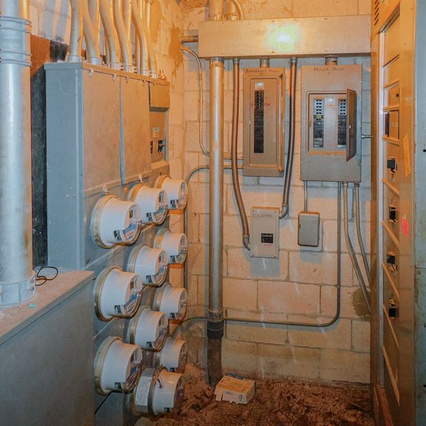 Electrical meters and circuit breaker boxes in a basement, with conduits and brick walls.
