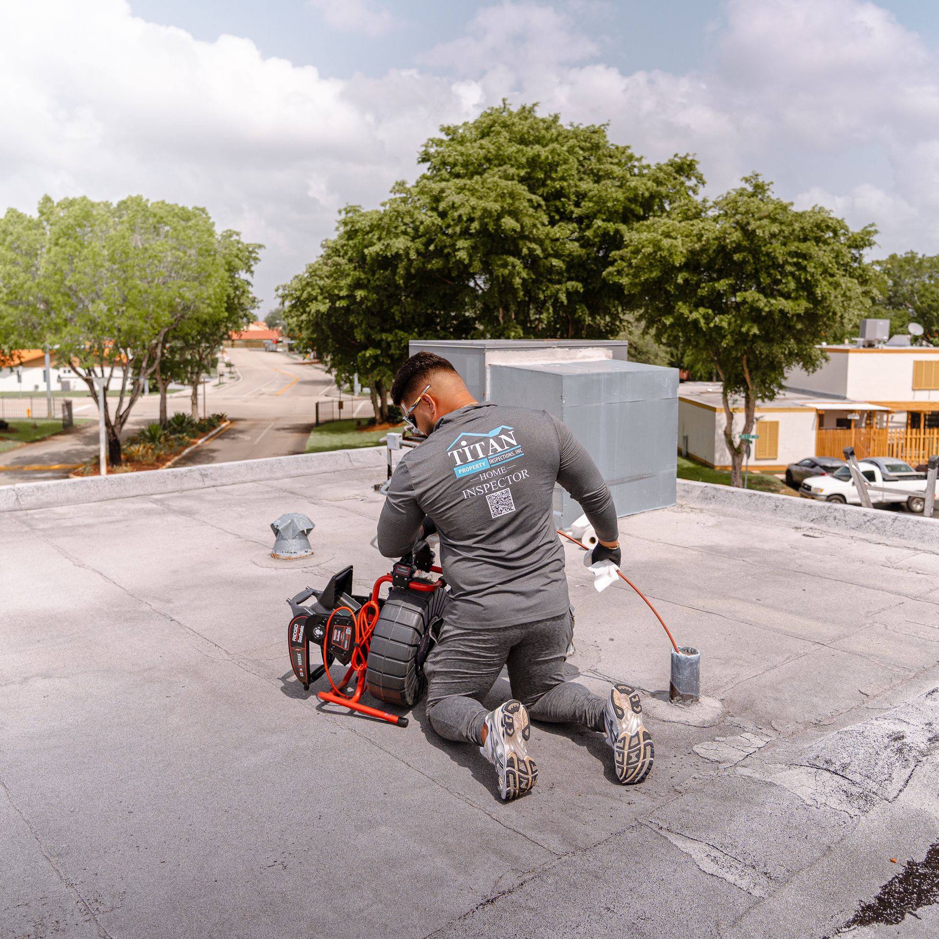 Hombre en un techo plano, operando una cámara de inspección de plomería, con árboles y edificios en el fondo.