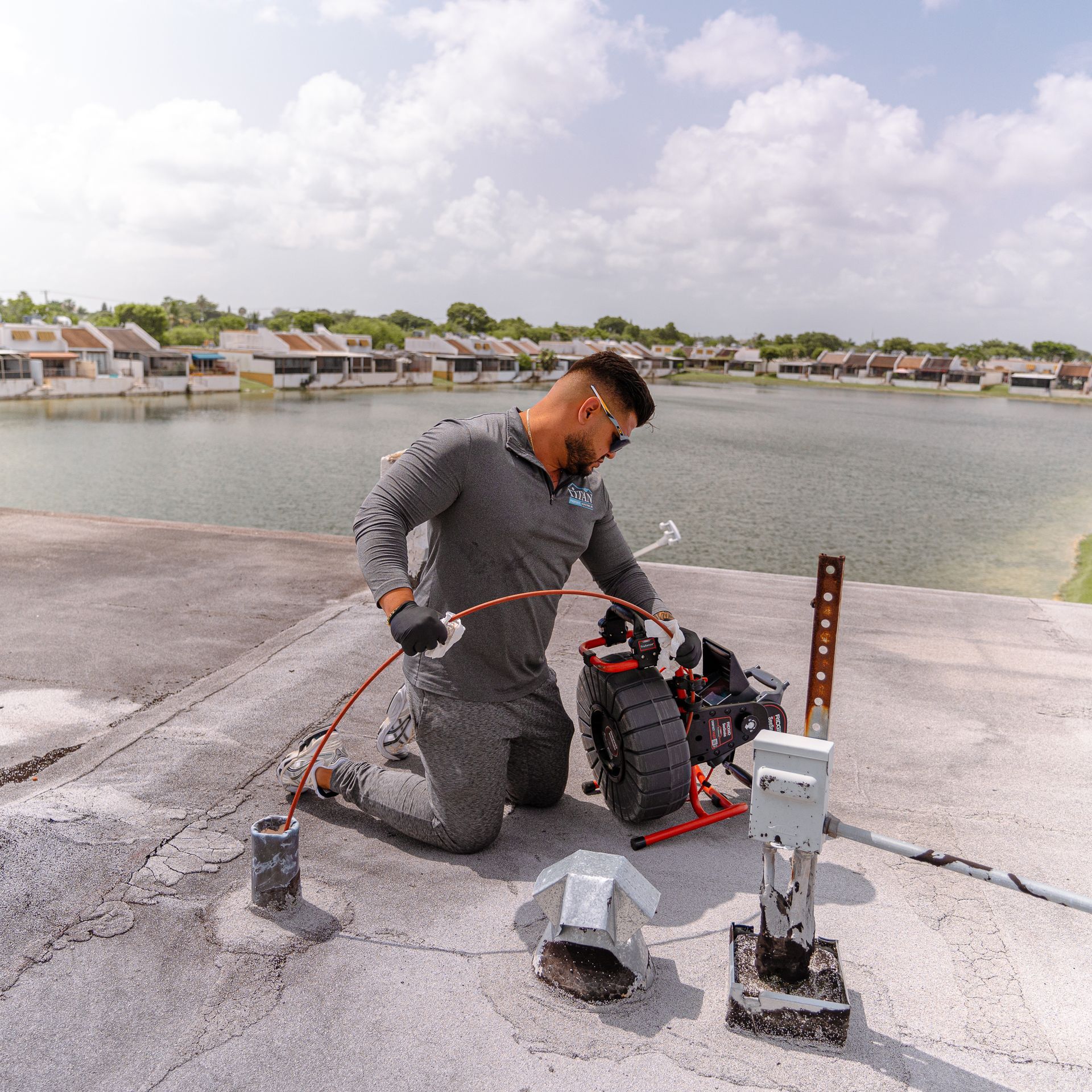 Persona en un tejado trabajando con maquinaria cerca del agua, día nublado.