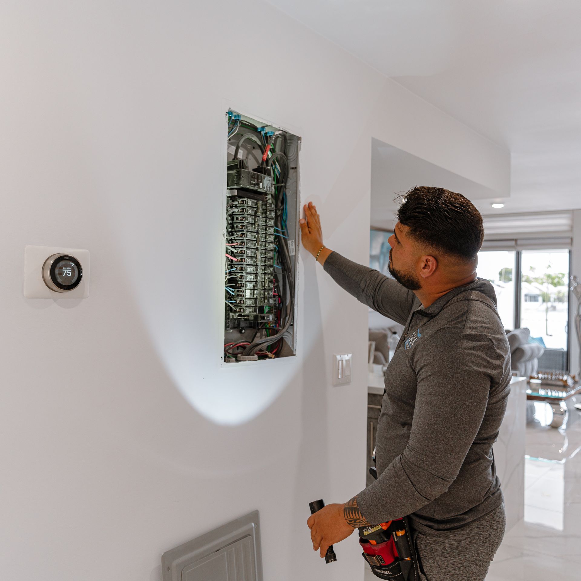 Electricista inspeccionando un panel eléctrico en una pared blanca en una casa moderna.