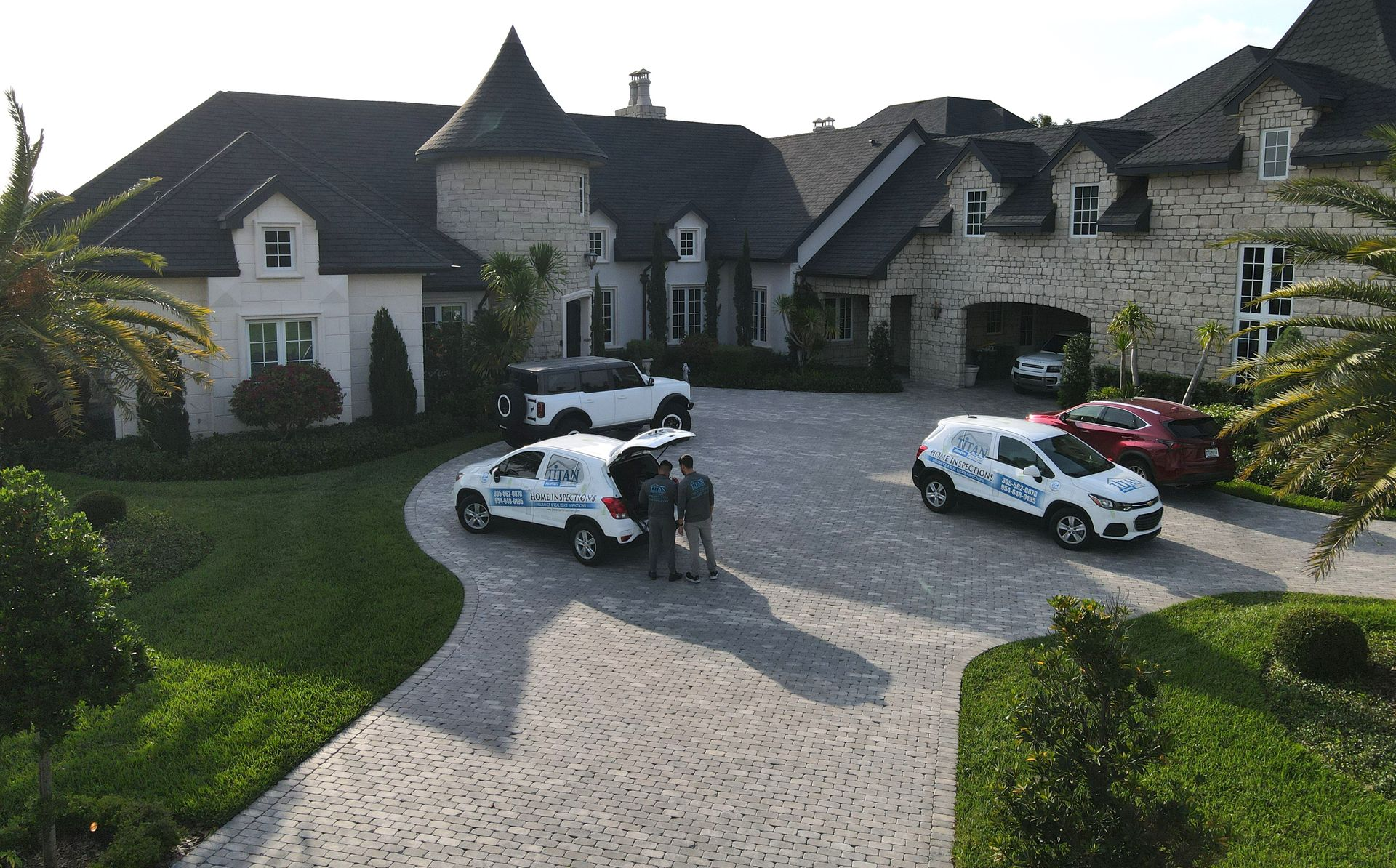 Two service vans parked in front of a large house with a circular driveway. Two people near one of the vans.