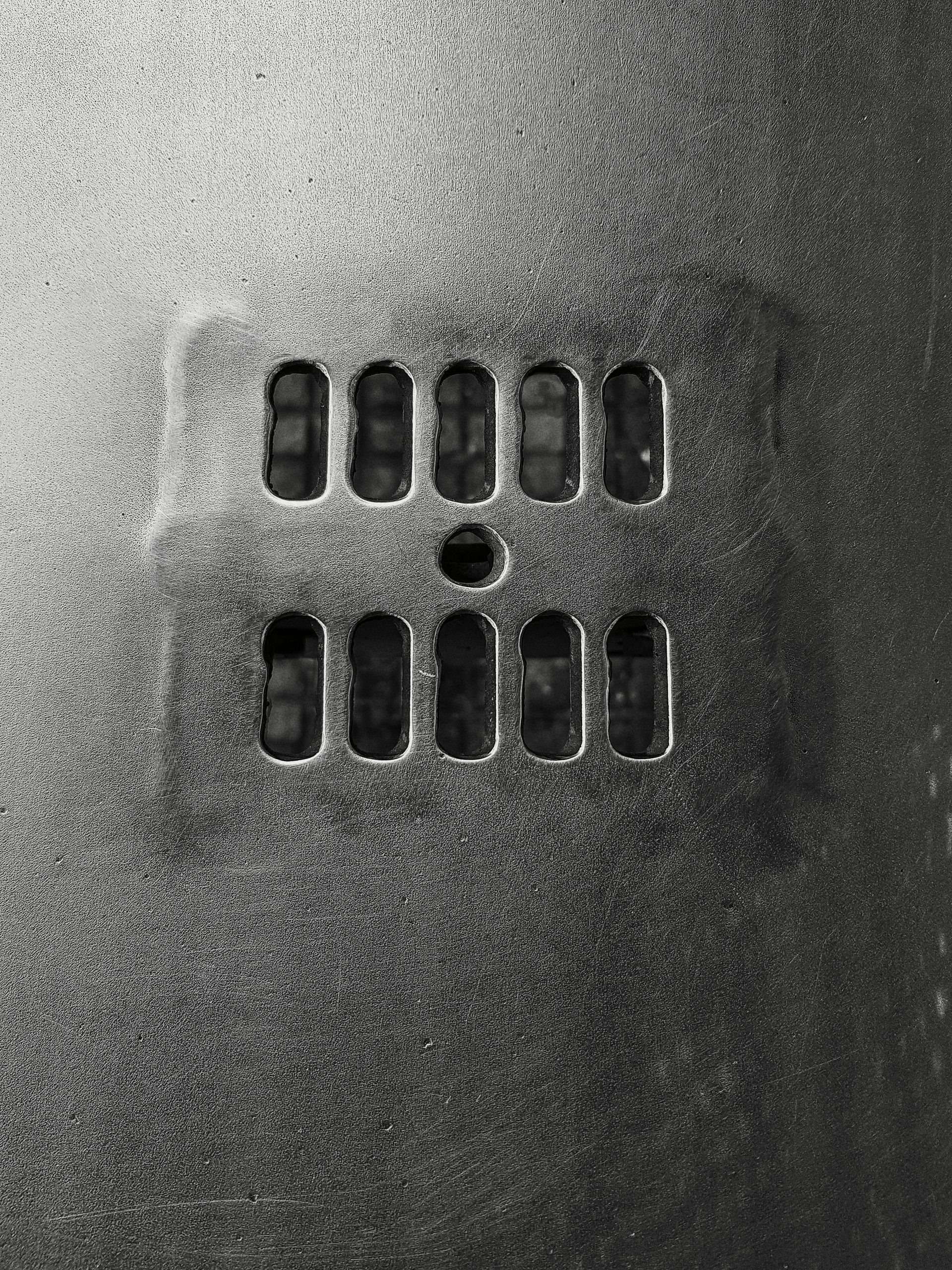 Panel metálico con filas de orificios de ventilación rectangulares y un orificio circular central.