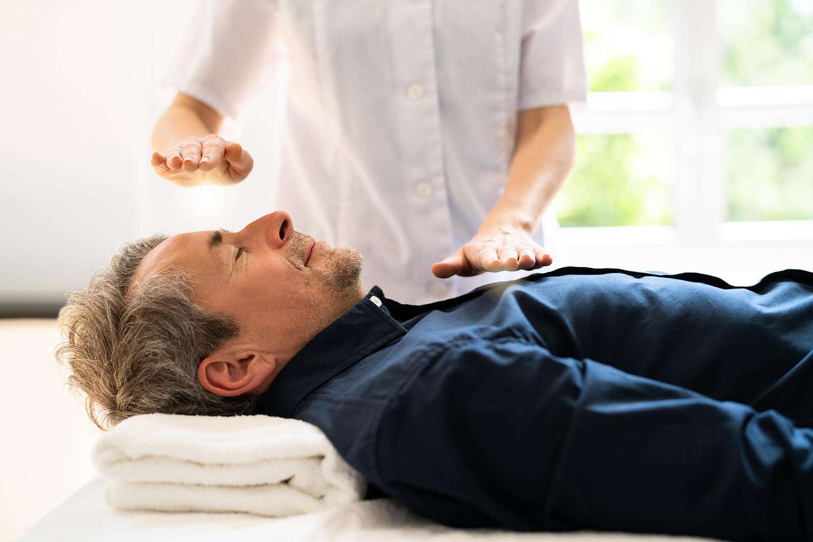 man with his eyes closed having Reiki healing treatment in wellness center