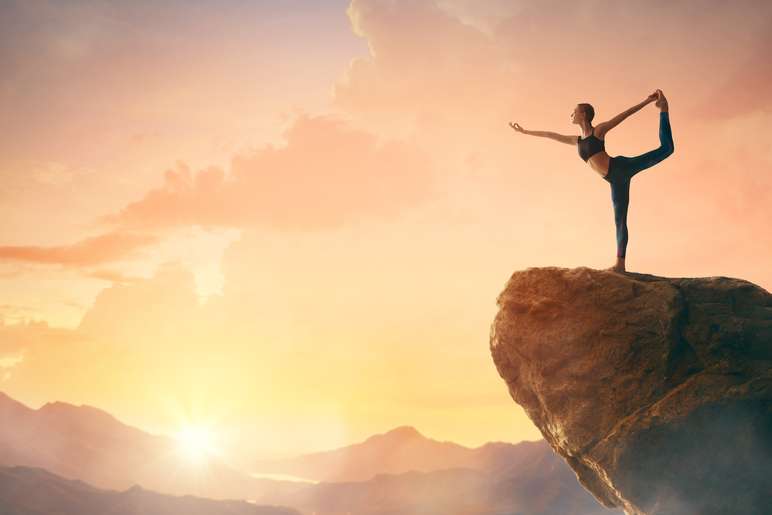 woman yoga posing on top of a big rock