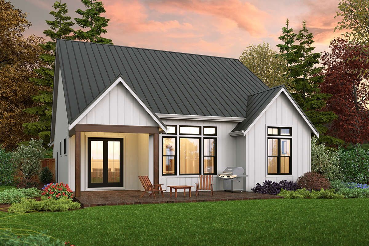 Small white house with gray roof, lit windows, front porch, and landscaped yard at sunset