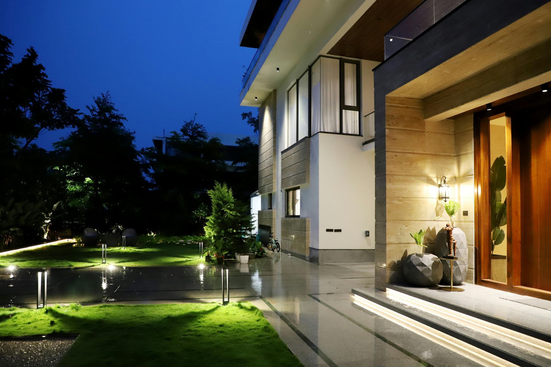 Modern house exterior at night with illuminated walkway and lawn.