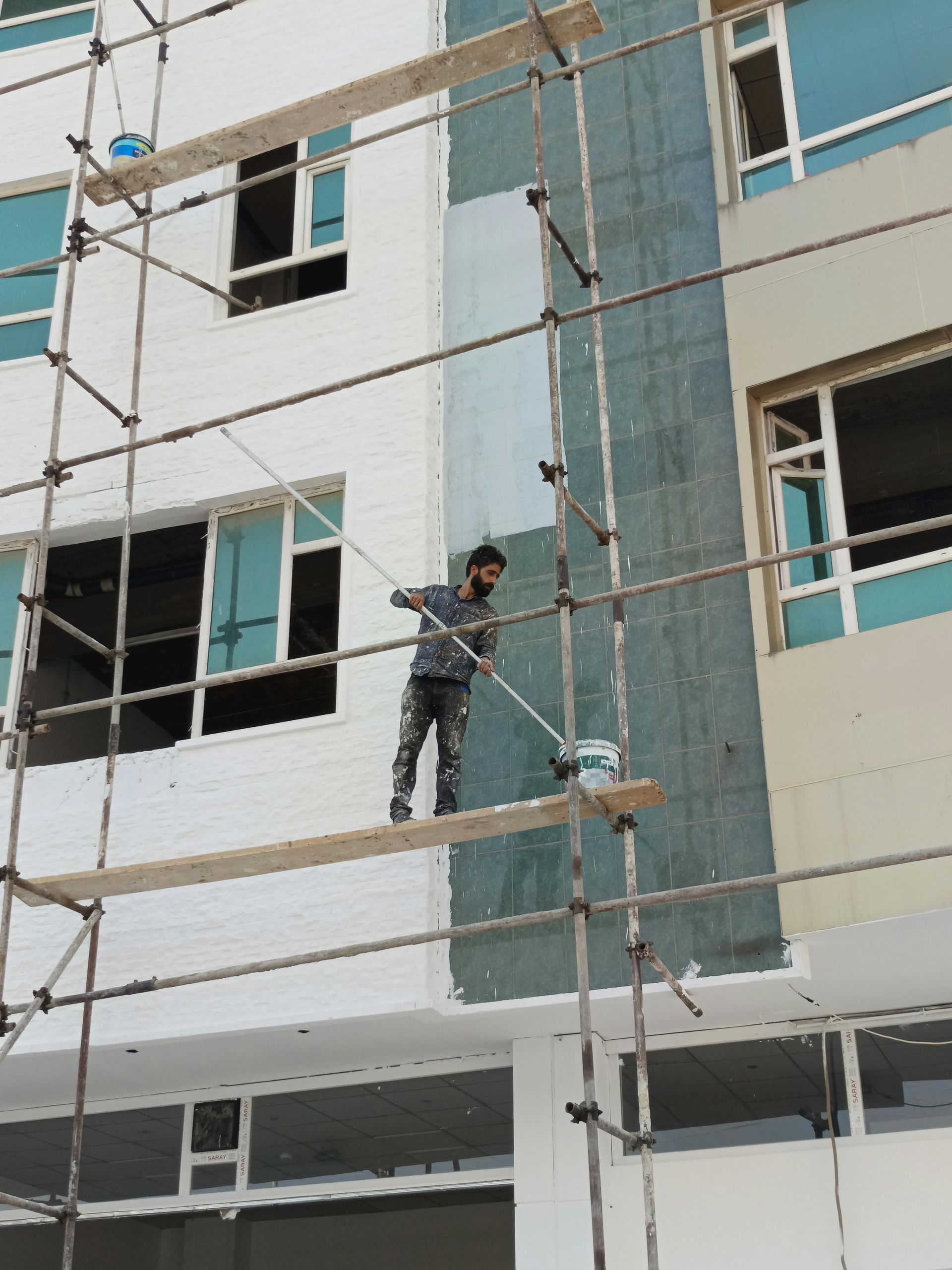 A person painting the exterior of a building while standing on scaffolding.