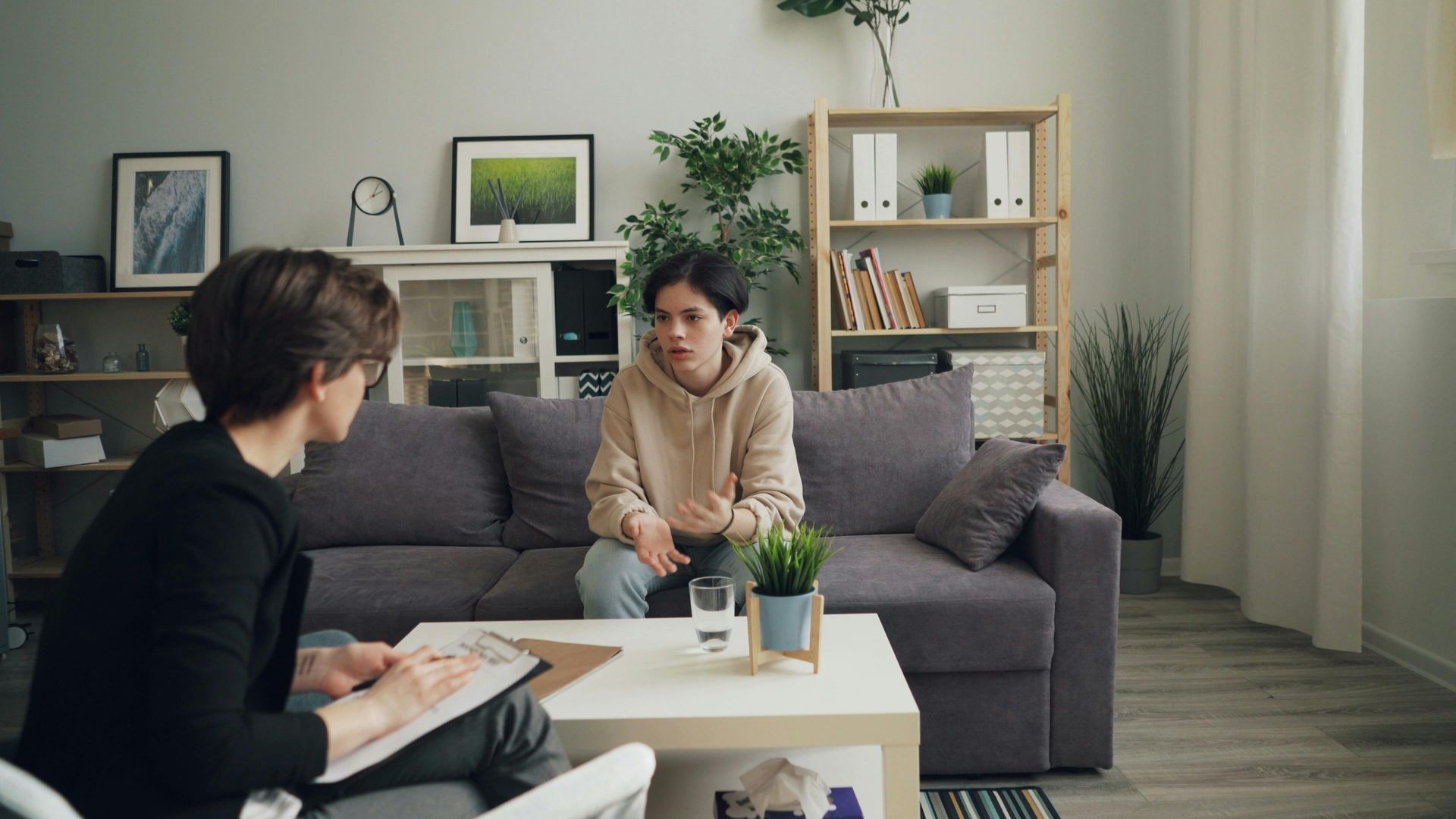 A person takes notes while sitting across from a person on a sofa during a consultation in a bright, modern office.