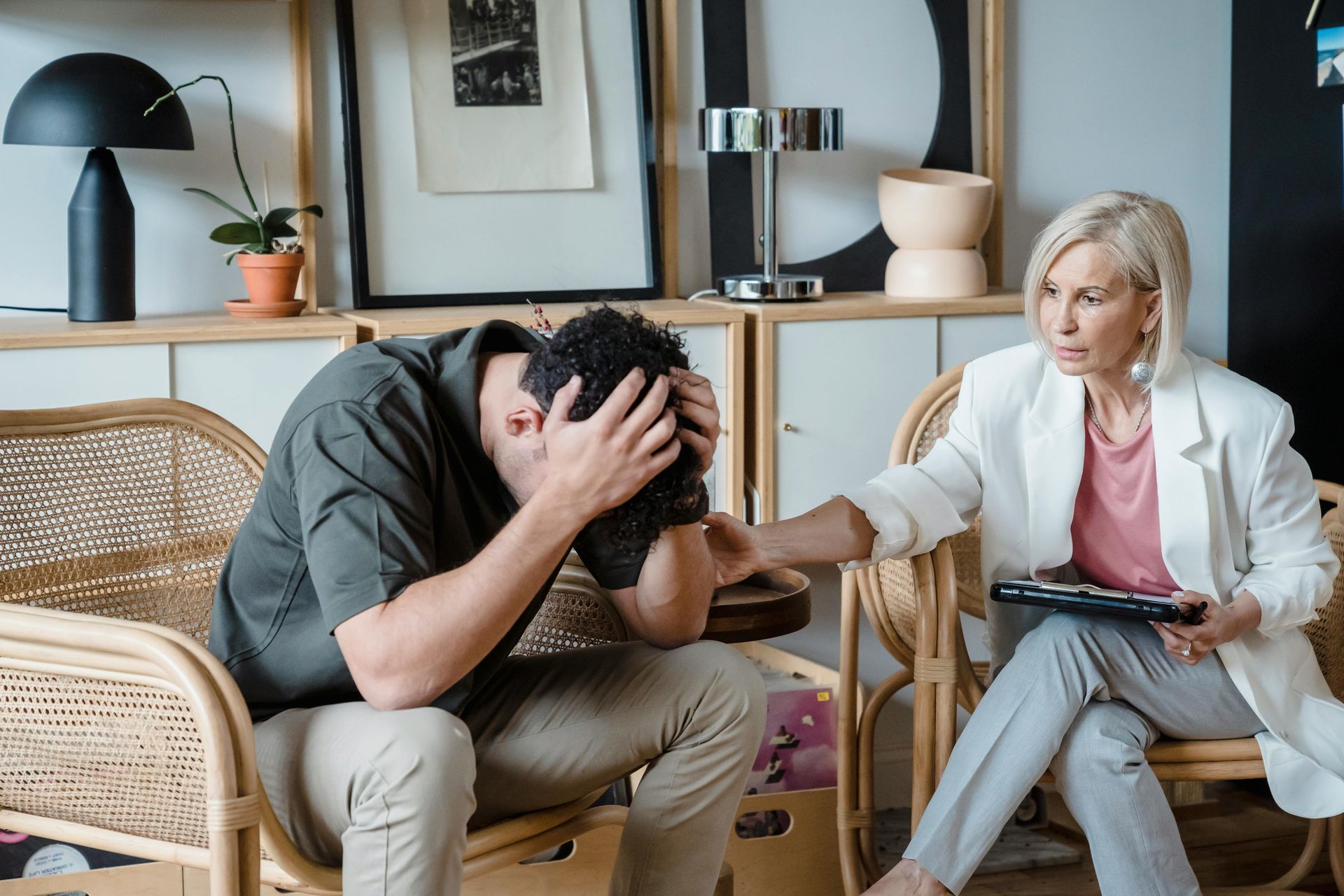 A professional providing comfort to a distressed person sitting with their head in their hands in a modern room.