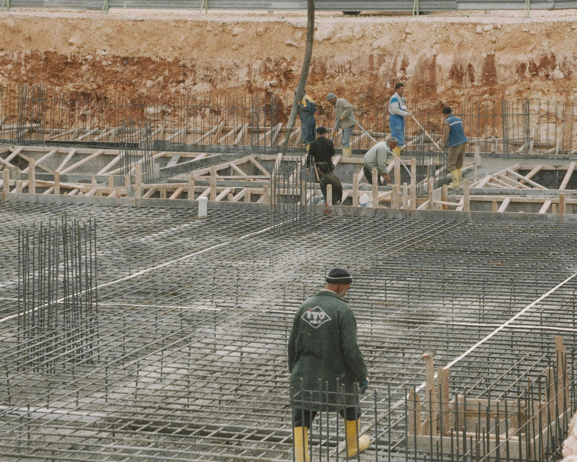 Workers on a large construction site, tying steel rebar for a concrete foundation.