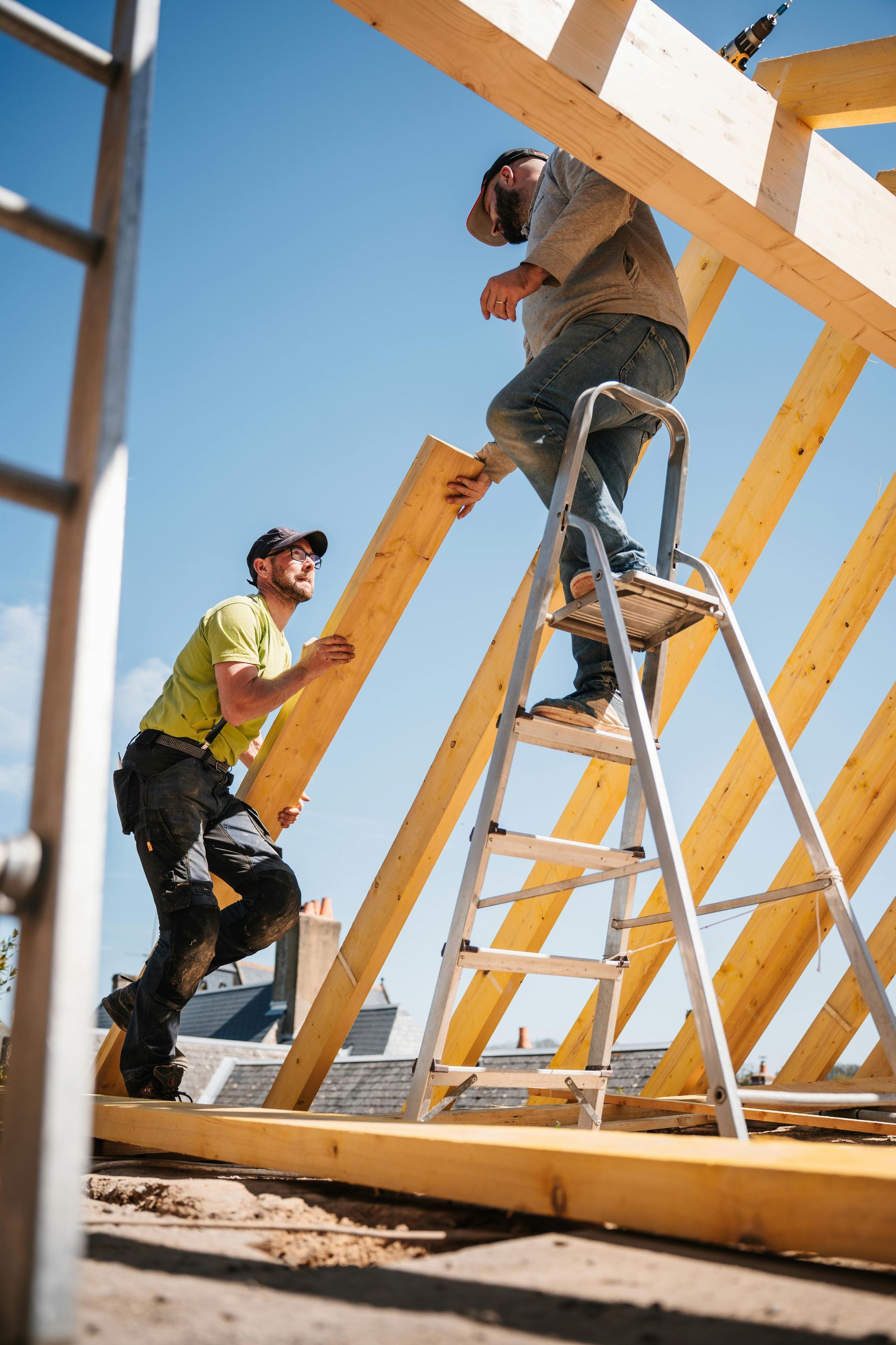 Two workers assembling a wooden frame at a construction site under a blue sky
