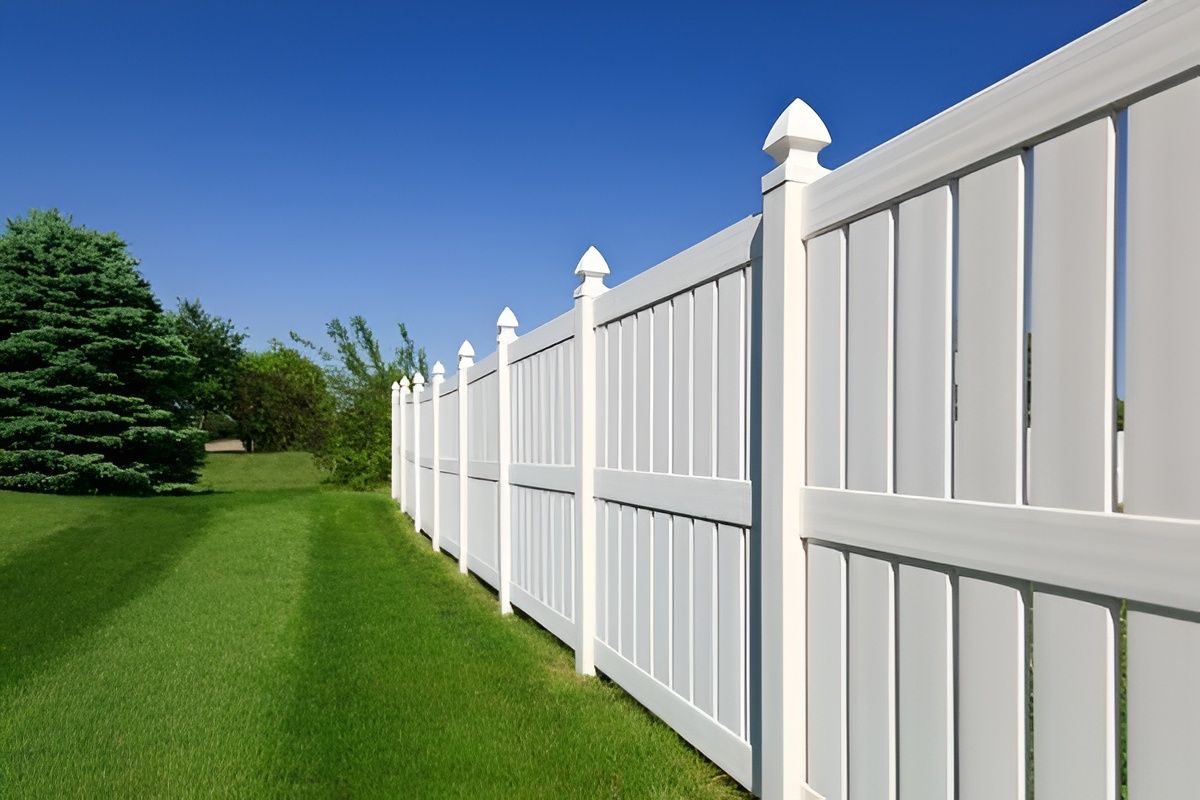 White vinyl fence with pointed post tops, along green grass and blue sky.