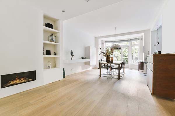 Bright white living room with fireplace, shelves, dining table, and hardwood floors.