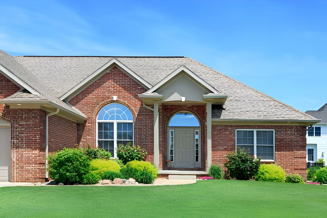 Brick house with green lawn, bushes, and a blue sky.