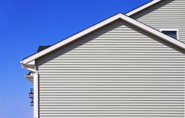 Side of a house with light gray siding, white trim, and a blue sky.