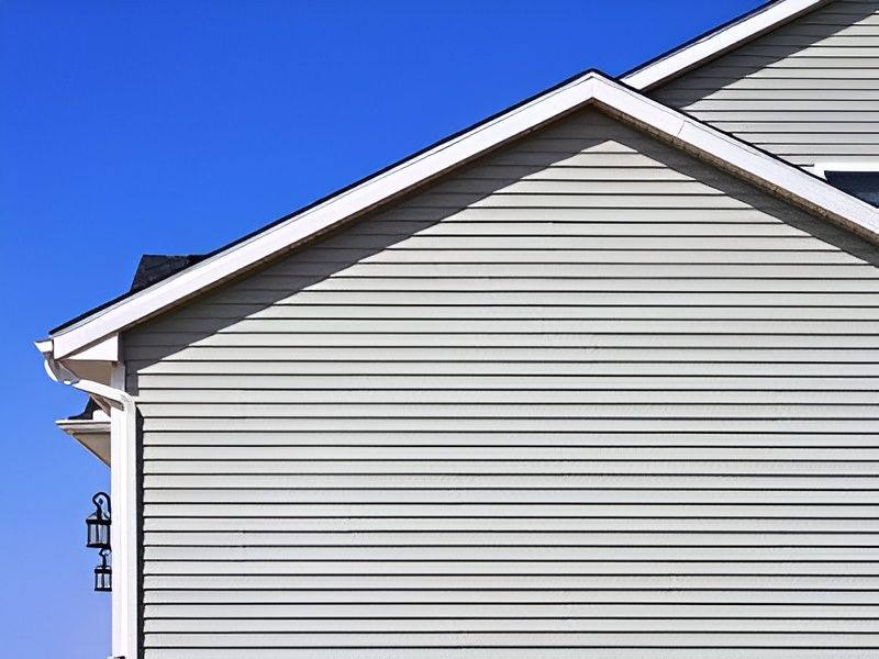 Side of a house with light gray horizontal siding, white trim, and a blue sky background.