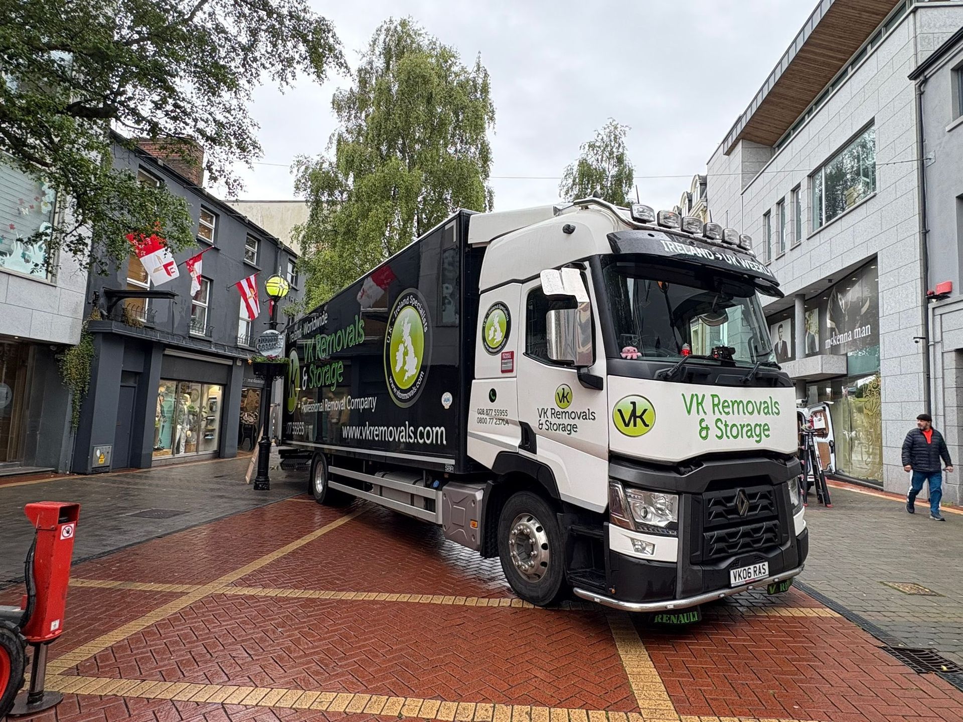 A removal truck parked on brick road next to a store, with trees and buildings in the background.