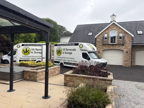 Two white vans are parked in front of a large house.