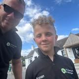 Two people wearing black polo shirts pose outdoors, one with sunglasses, both smiling.