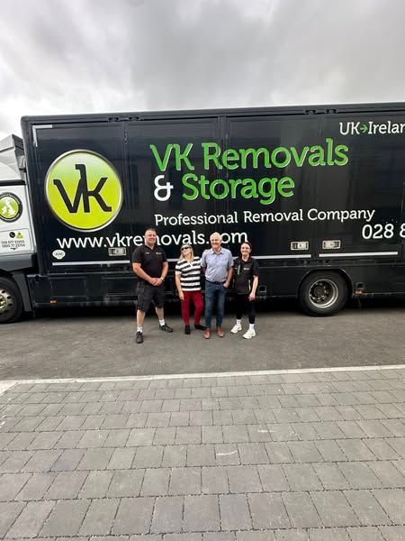 Four people stand in front of a black VK Removals truck. They appear to be smiling.