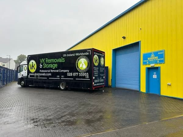 Black moving truck outside a yellow building with a blue door and a loading bay.