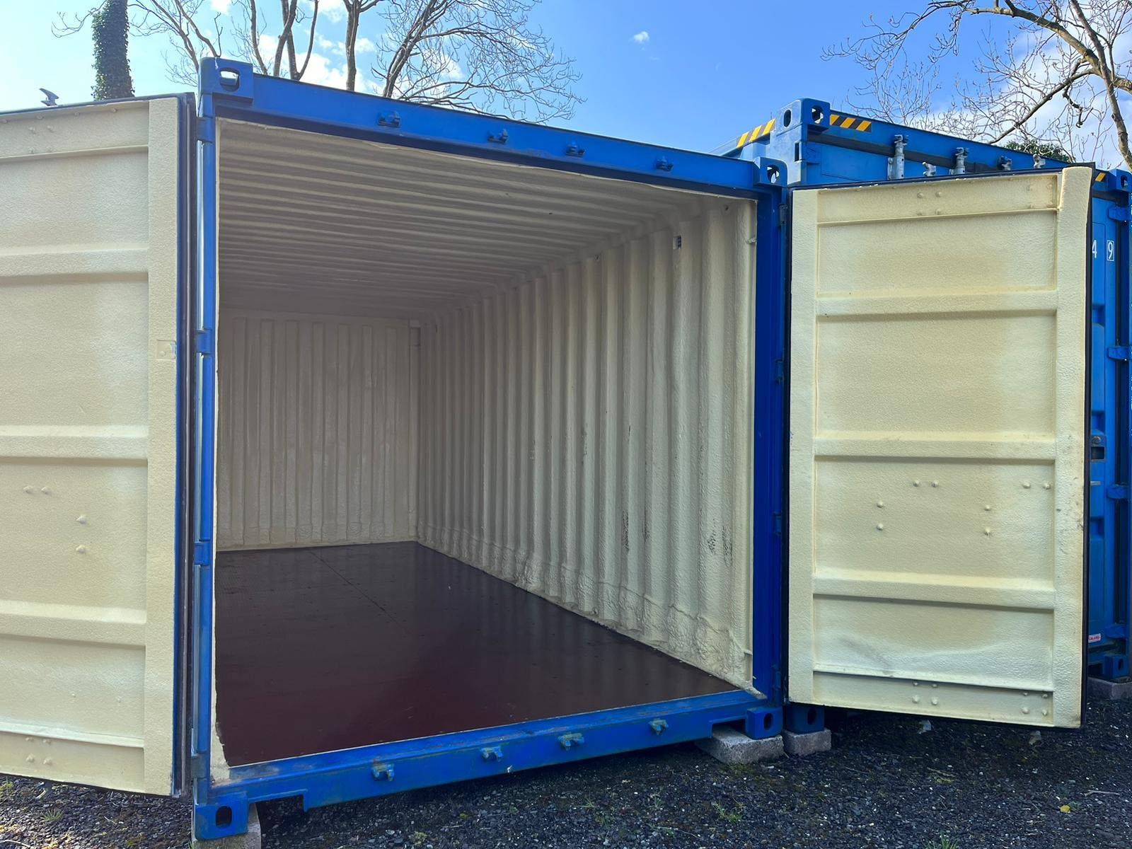 Blue shipping container interior, insulated with tan foam, doors open.