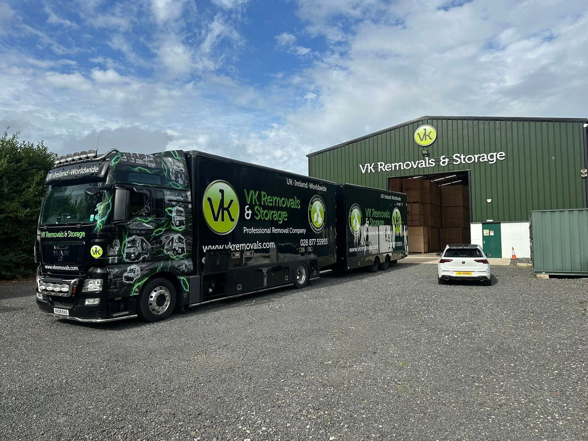 Large black and green VK Removal & Storage truck parked in front of a storage facility.