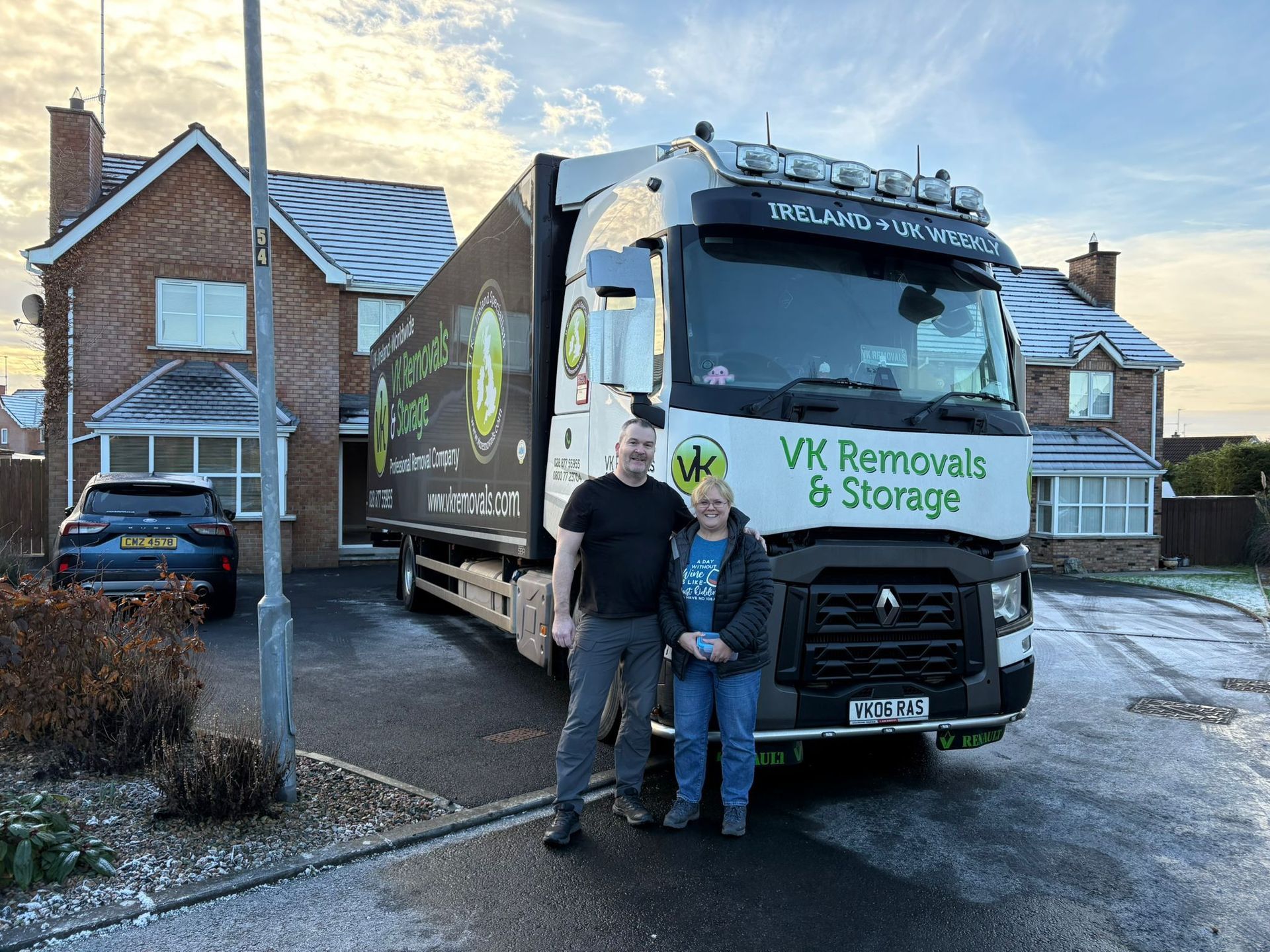 A family stands in front of a moving truck in a snowy residential area, ready to move.