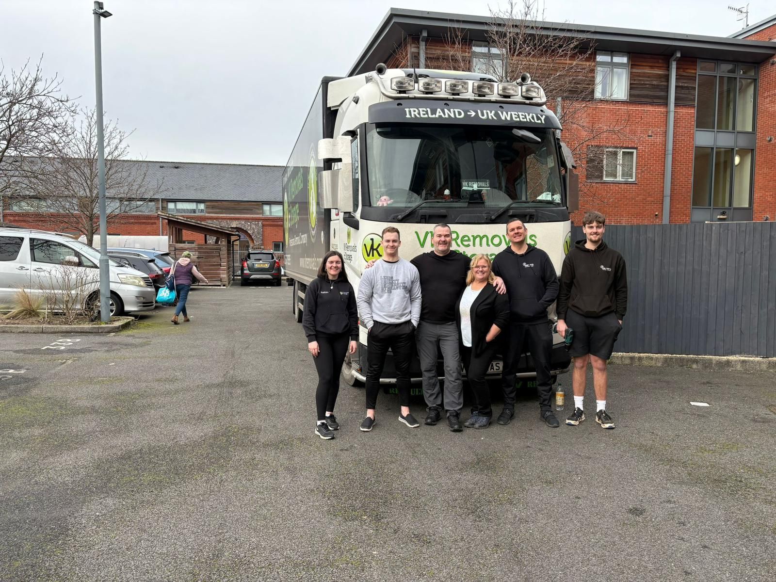 Three people posing in front of a large white moving truck with business branding in a parking lot.