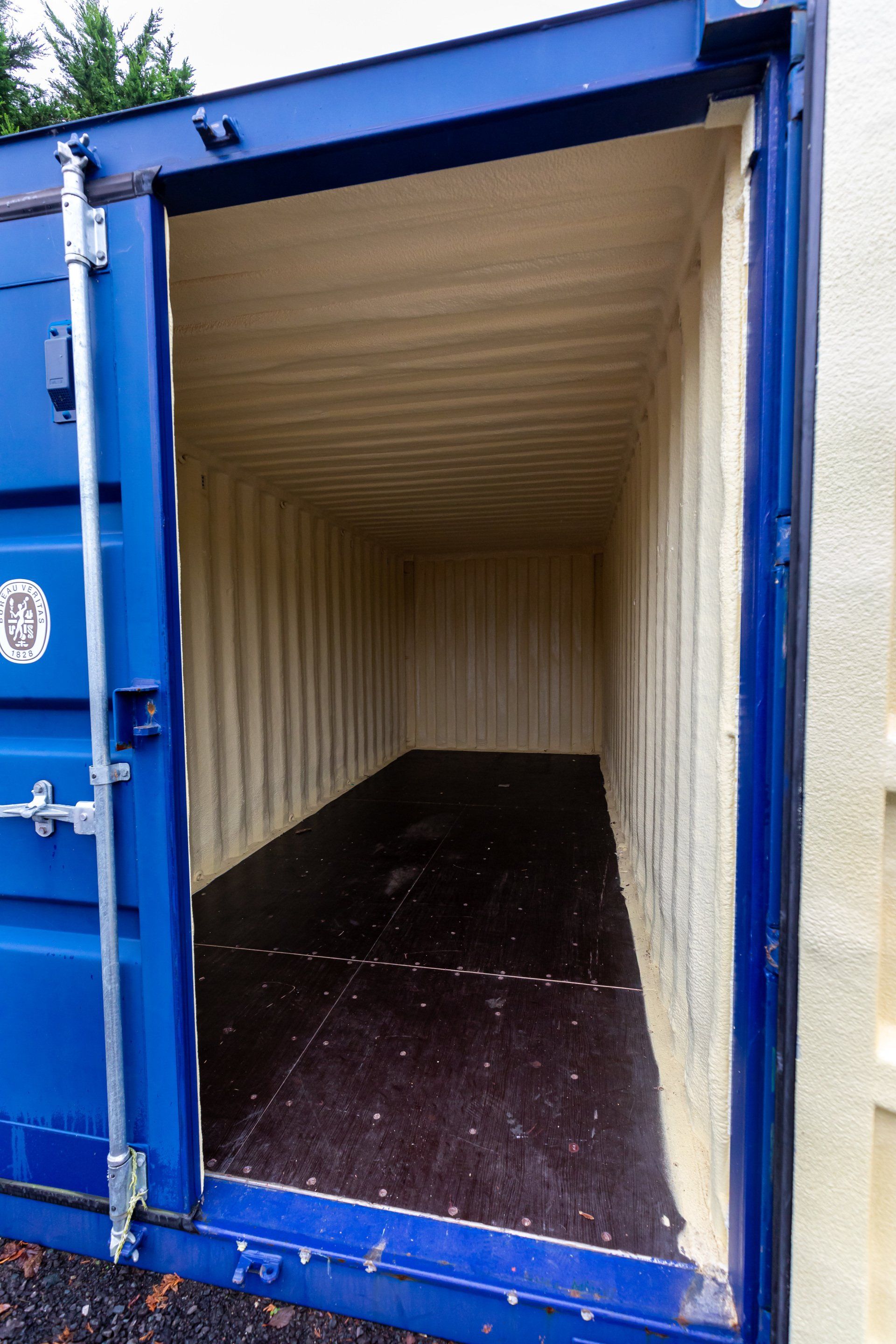 Blue shipping container interior with tan insulation and dark floor, viewed from open doors.